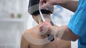 Male physician applying Y-shaped tapes on female patient upper back, healthcare