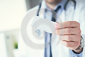 Male physician hand holding and giving white blank calling card closeup in office. Contact information exchange