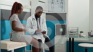 Male physician taking notes at checkup visit with pregnant woman