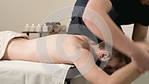 A male physiotherapist does a power stretching for a male patient to a young bearded hipster in a medical massage room