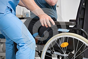 Male Physiotherapist helping a patient with a disability who uses a wheelchair to get up at rehabilitation hospital.