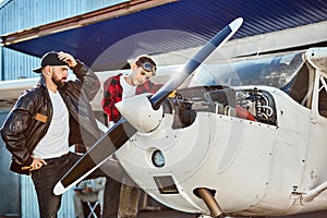 Male pilot and his son standing near opened engine block, searching for reason of failure