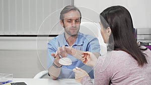Male plastic surgeon showing silicone breast implants to a patient
