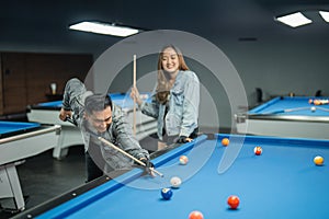 male player poking the white ball with the female player standing behind