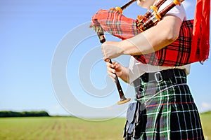 Male playing Scottish traditional pipes on green