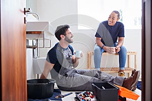 Male Plumber With Female Apprentice Taking A Break From Fixing Leaking Sink In Home Bathroom