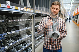 male plumber in a hardware store chooses the sewer pipes, the concept of plumbing work in the house