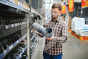 male plumber in a hardware store chooses the sewer pipes, the concept of plumbing work in the house