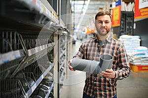 male plumber in a hardware store chooses the sewer pipes, the concept of plumbing work in the house