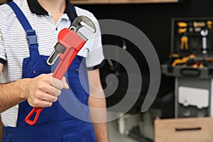 Male plumber holding pipe wrench in kitchen, closeup. Repair service