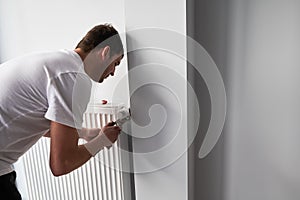 Male plumber installing heating radiator in apartment.