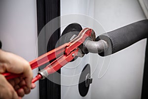 male plumber with pipe wrench installs a new pellet heater in the basement