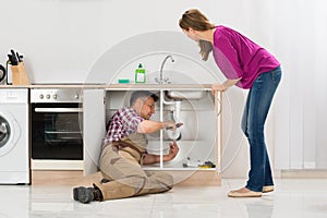 Male Plumber Repairing Pipe Under Sink In Kitchen