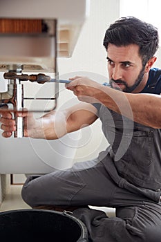 Male Plumber Using Wrench To Fix Leaking Sink In Home Bathroom