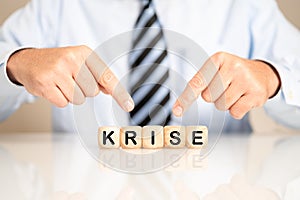 Male pointing to wooden cubes with the letters making the German word Krise meaning crisis