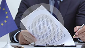 Male politician attentively reading memorandum, European Union flag on table