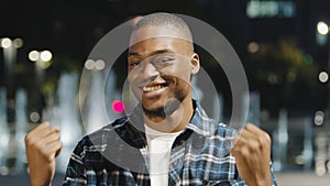 Male portrait african american man guy in plaid shirt stands in city in evening at night looking at camera says wow