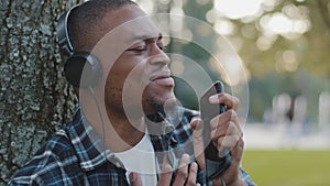 Male portrait african american young guy funny man in headphones listening to music using phone online radio pretending