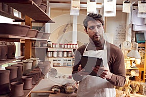 Male Potter In Ceramics Studio Checking Orders Using Digital Tablet