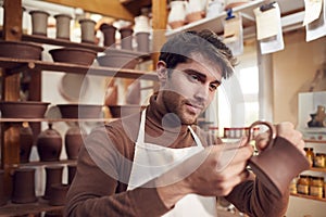 Male Potter Fitting Clay Handles To Mugs In Ceramics Studio