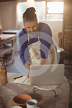 Male potter working on laptop