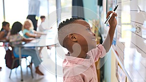 Male Primary Or Elementary School Student Writing On Whiteboard In Classroom Lesson