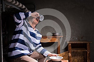 Male prisoner drinking from an aluminum cup in a small prison ce