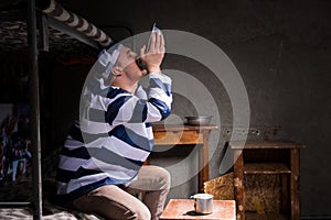 Male prisoner sitting on a bed and eating from aluminum plate in