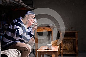 Male prisoner sitting on a bed and licking aluminum plate in a s