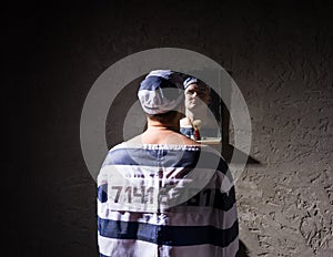 Male prisoner standing and looking at his reflection in the mirror in a prison cell