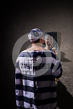 Male prisoner standing with toothbrush and looking at his reflection in the mirror in a prison cell