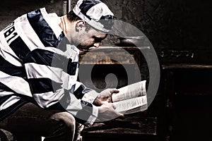 Male prisoner wearing prison uniform reading a book or a bible w