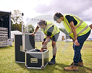 Male Production Team Unpacking Flight Case And Setting Up Outdoor Stage For Music Festival 