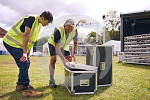 Male Production Team Unpacking Flight Case And Setting Up Outdoor Stage For Music Festival 