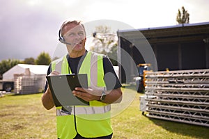 Male Production Worker With Headset Setting Up Outdoor Stage For Music Festival Or Concert