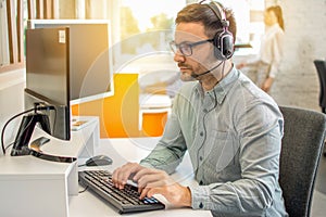 Male professional call center telesales agent wearing headset using computer in customer care support service office