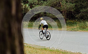 A male professional cyclist rides on the road through the woods and trains outside the city