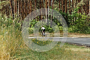 A male professional cyclist rides on the road through the woods and trains outside the city