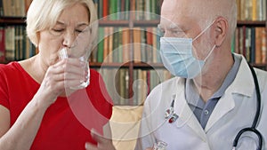 Male professional doctor at work. Senior man physician treat senior female patient giving flu pill