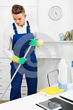 Male professional janitor dusting in office