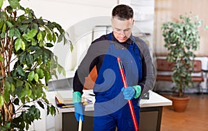 Male professional janitor dusting in office interior