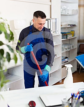 Male professional janitor dusting in office interior