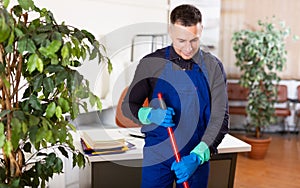Male professional janitor dusting in office interior