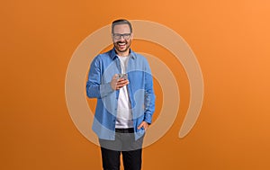 Male professional laughing and checking social media apps over mobile phone on orange background