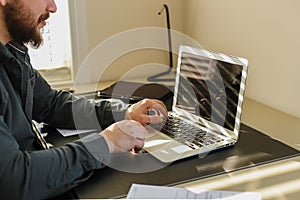 Male programmer writing program at office on laptop, typing on keyboard.