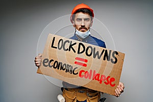 Male protester holding placard against coronavirus lockdowns against grey background