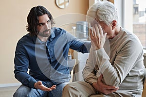 Male psychologist comforting senior man crying in mental health support group