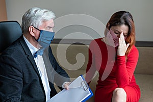 Male psychotherapist advises a female client in a medical mask. Moral support during the epidemic. Depressed woman on a