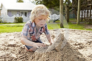 Male Pupil At Montessori School Playing In Sand Pit At Breaktime