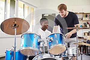 Male Pupil With Teacher Playing Drums In Music Lesson